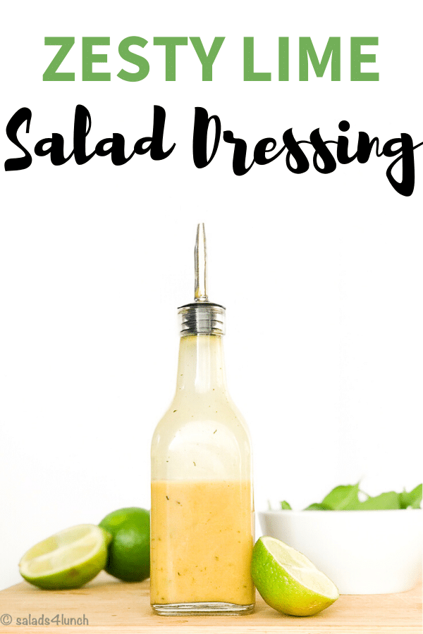 Zesty lime salad dressing in a bottle on a wooden board with white bowl of spinach and cut lime slices, zesty lime salad dressing text overlay