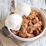 Fresh hot homemade apple crisp or crumble with crunchy streusel topping topped with vanilla bean ice cream. Selective focus with blurred background.
