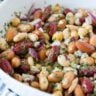 Close up of a white bowl with five bean salad in it on a blue and white striped napkin.