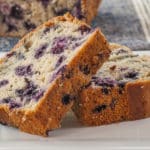 Close up of two slices of blueberry lemon load on a white plate with a blue linen napkin in the background
