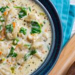 Close up of creamy gnocchi bacon soup in a blue bowl on a white table with blue napkin.