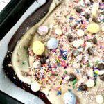 Chocolate Easter Bark in a pan with a hand holding Cadbury Mini Eggs