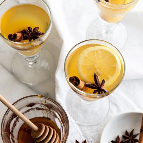 Three glasses of green tea hot toddy next to a jar of honey.