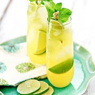 Two pineapple limeade coolers in tall glasses with fresh cut lime slices.