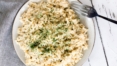 Photo showing close up of plate with Instant Pot Creamy Garlic Parmesan Risotto on a white background with a light grey napkin