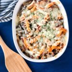 Penne pasta with hearty meat sauce with melted mozzarella cheese in a white casserole dish on a blue background