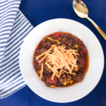 Overhead of of keto chili toppped with cheese in white bowl on blue placemat.