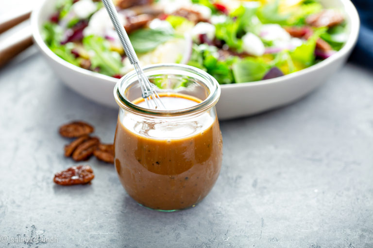 Wide photo of balsamic vinaigrette in a mason jar next to a salad in a white bowl.