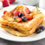 Two slices of Classic french toast with blueberries and strawberries on a white plate.