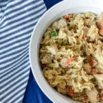 White casserole dish on a blue placemat with blue striped napkin with creamy chicken noodle casserole loaded with tender carrots and celery.
