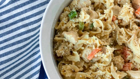 White casserole dish on a blue placemat with blue striped napkin with creamy chicken noodle casserole loaded with tender carrots and celery.
