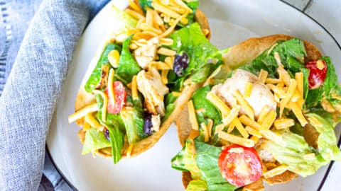 Two crispy edible taco bowls with chipotle chicken salad in them on a square white plate with black trim and a grey napkin beside the plate.