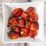Close of square white bowl full of bacon wrapped water chestnuts appetizers.