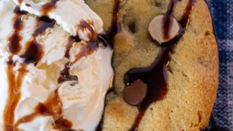Close up of Salted Caramel and Chocolate Chip SKillet Cookie topped with vanilla ice cream and drizzled with chocolate on a blue and white plaid napkin.