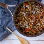 Silver skillet with Mexican Rice Casserole on a blue linen napkin with a wooden spoon to the left of the skillet,
