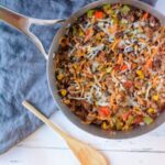 Silver skillet with Mexican Rice Casserole on a blue linen napkin with a wooden spoon to the left of the skillet,