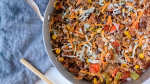 Silver skillet with Mexican Rice Casserole on a blue linen napkin with a wooden spoon to the left of the skillet,
