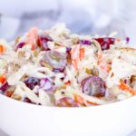 Close up of the best ever creamy coleslaw recipe with grapes in a white bowl on a white wooden table.