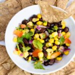 Overhead photo of Corn and Black Bean Salsa in a small white bowl surrounded by black bean chips.