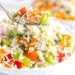 Close up of basmati rice salad with peppers, celery, mint and edamame on a white plate.