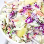 Close up of colourful hawaiian coleslaw with pineapple in a white bowl.