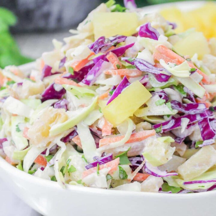 Close up of colourful hawaiian coleslaw with pineapple in a white bowl.