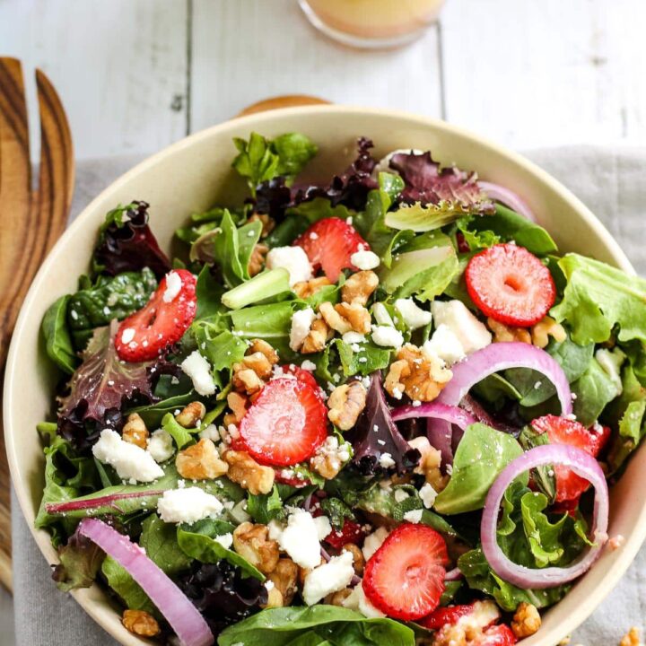Strawberry feta and mint salad with fresh greens in a white bowl with a wooden salad fork next to the bowl.