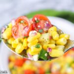 Summer corn salad on a spoon showing juicy corn kernels, red onion, cherry tomato halves and feta cheese.