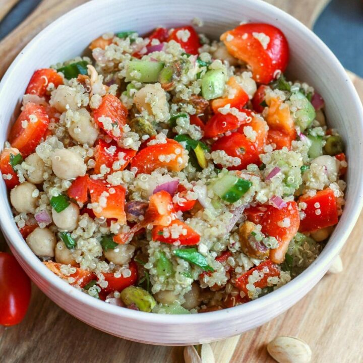 Close up of a very colourful quinoa salad in a white bowl on a cutting board.