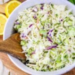 White bowl with colorful creamy blue cheese coleslaw in it with yellow lemons in the background.