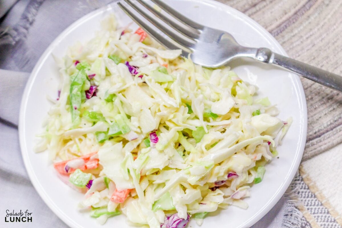 Classic coleslaw salad with mayonnaise on a white plate with a fork.