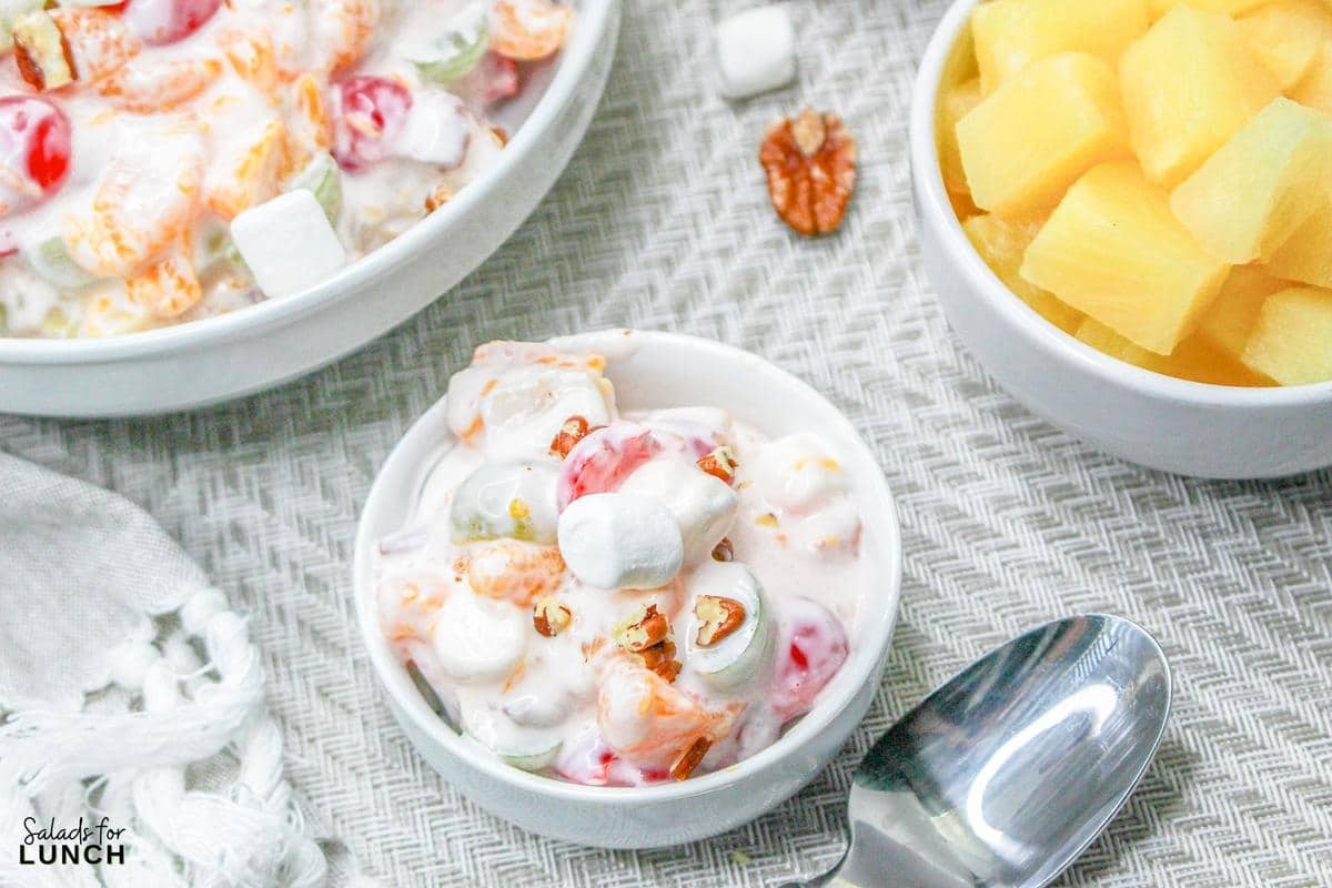 Ambrosia Salad without Coconut in a white bowl with pineapple and a spoon.