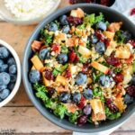 a lively mix of blueberries, cranberries, apple, quinoa, and kale is beautifully presented in a grey bowl on a wooden board, offering a visual feast and a nutritious delight.