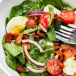 A spinach salad with bacon, eggs, tomato and onion in a bowl.