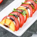 A plate of sliced peaches, tomatoes and cheese with mint leaves and drizzled with balsamic glaze