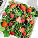 A salad with arugula,berries and honey roasted pecans topped with a creamy balsamic vinaigrette on a plate.