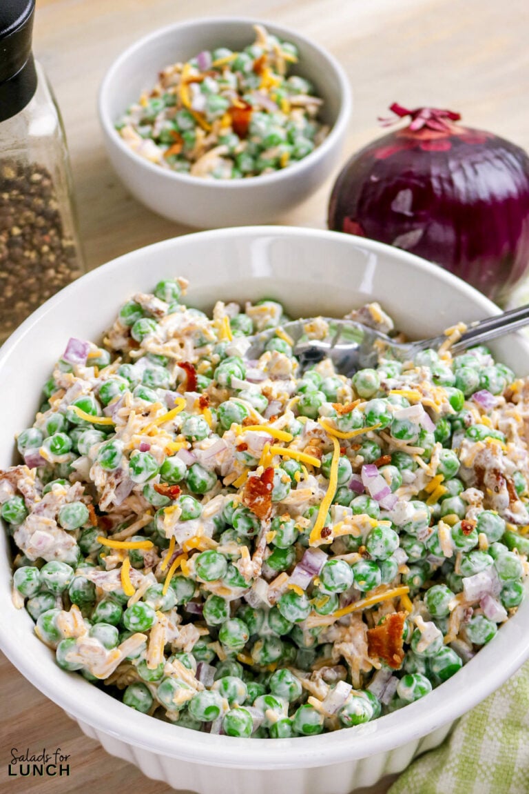 Pea salad made with sour cream, bacon, cheese and red onion in a white bowl.