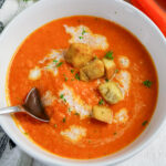 Creamy carrot soup in a white bowl, topped with croutons and parsley. Carrots on the side.