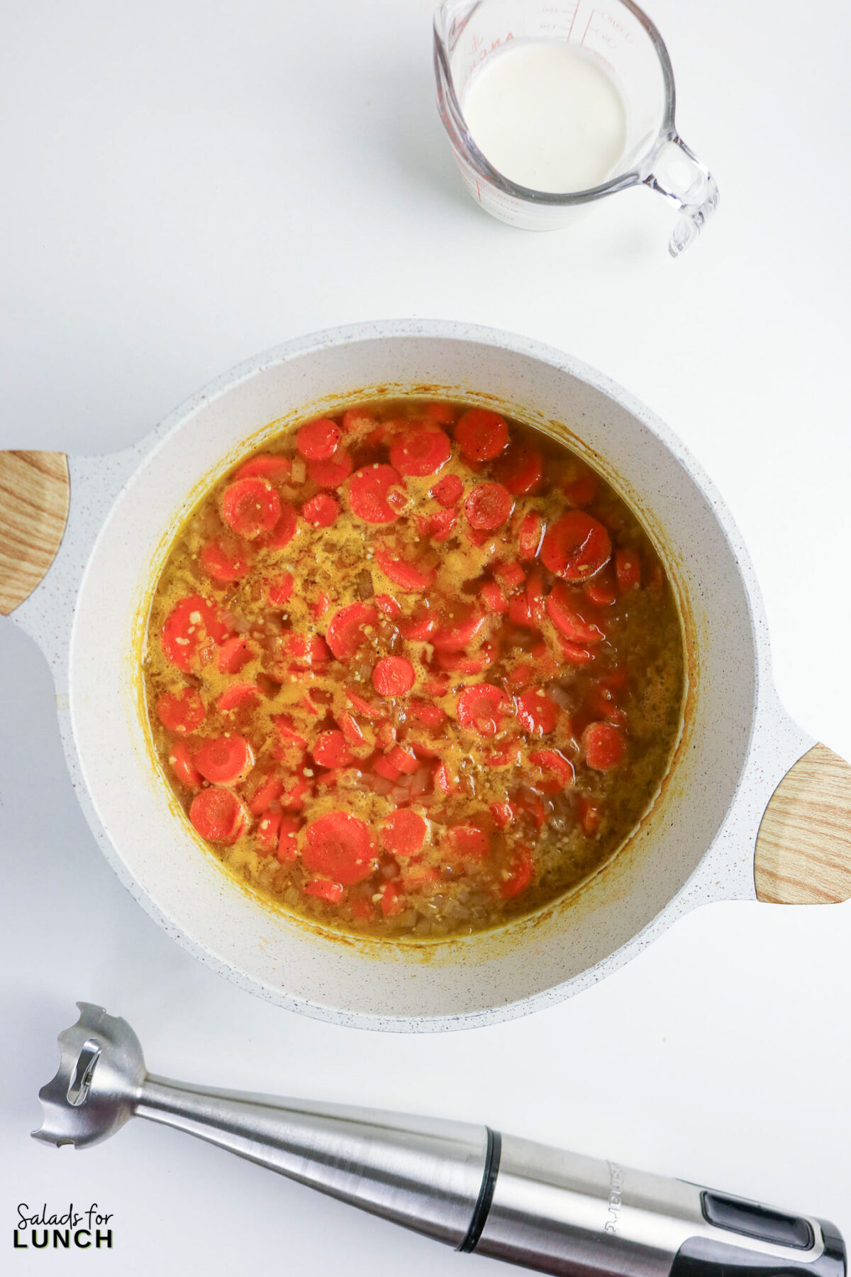 Creamy carrot soup in a pot with cream and immersion blender.