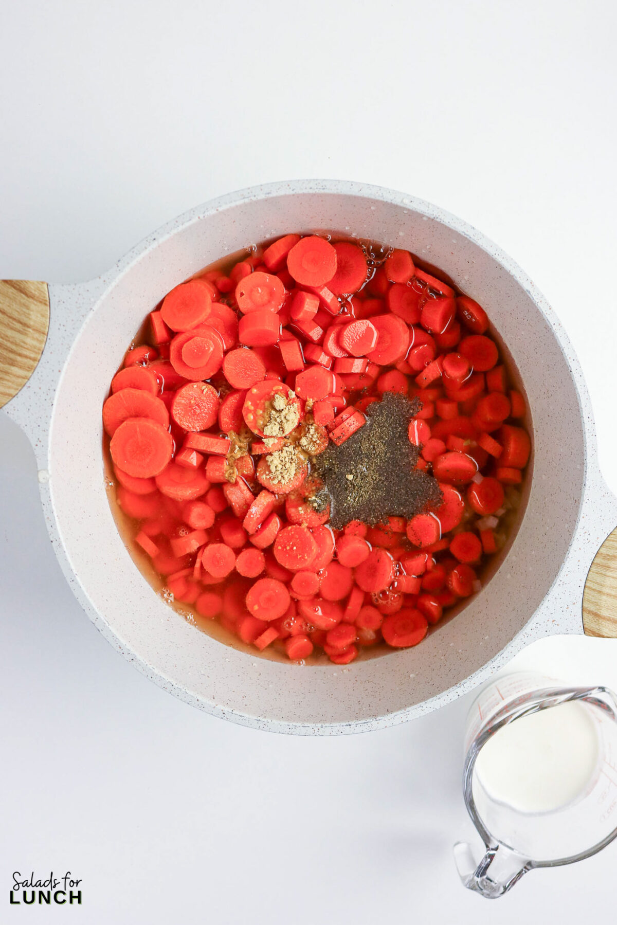 Creamy carrot soup ingredients in pot: sliced carrots, spices, and broth ready to cook.