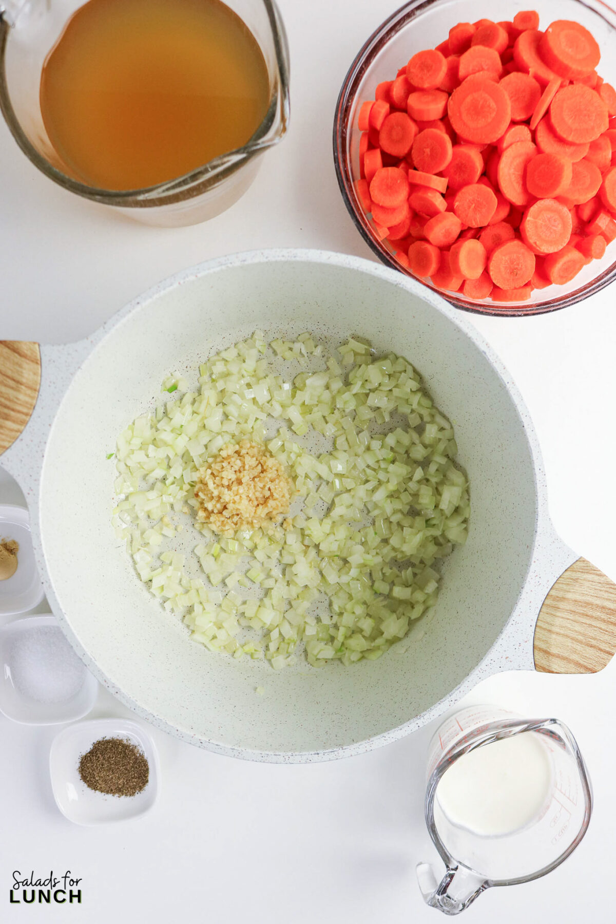 Ingredients for creamy carrot soup: diced onions and garlic sautéing in a pot, carrots, broth, and cream ready to be added.