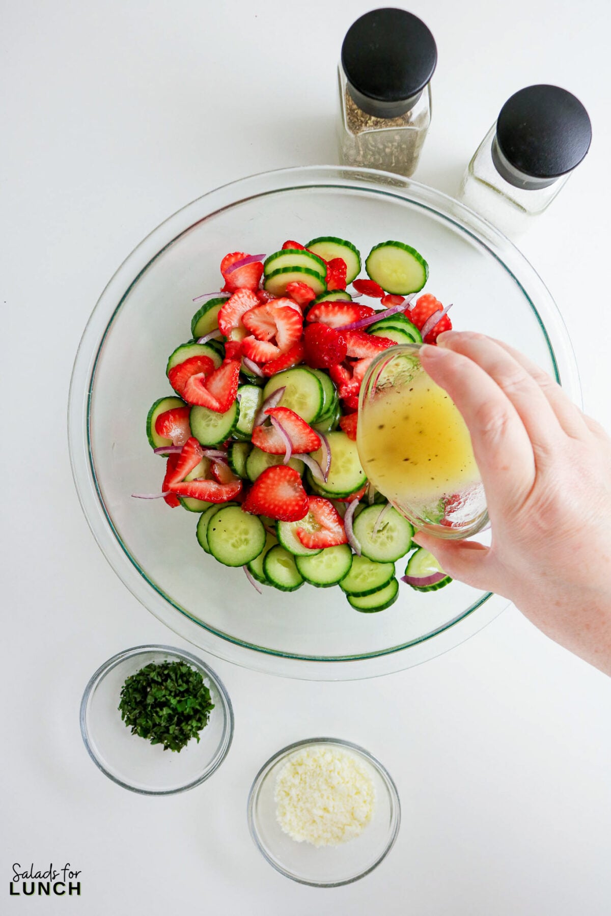 Strawberry Cucumber Salad being dressed, with feta and mint nearby.