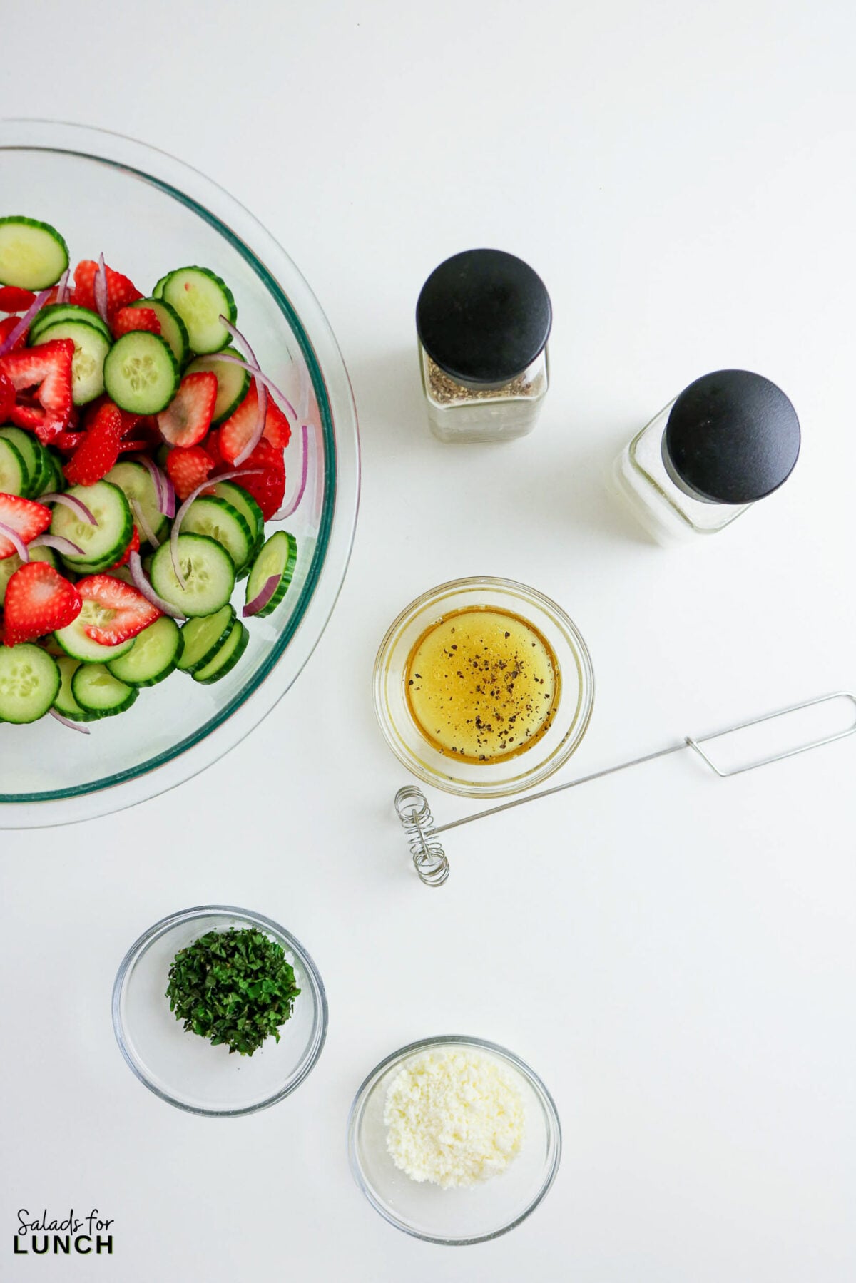Strawberry cucumber salad ingredients: bowl with salad, dressing, herbs, feta, spices.