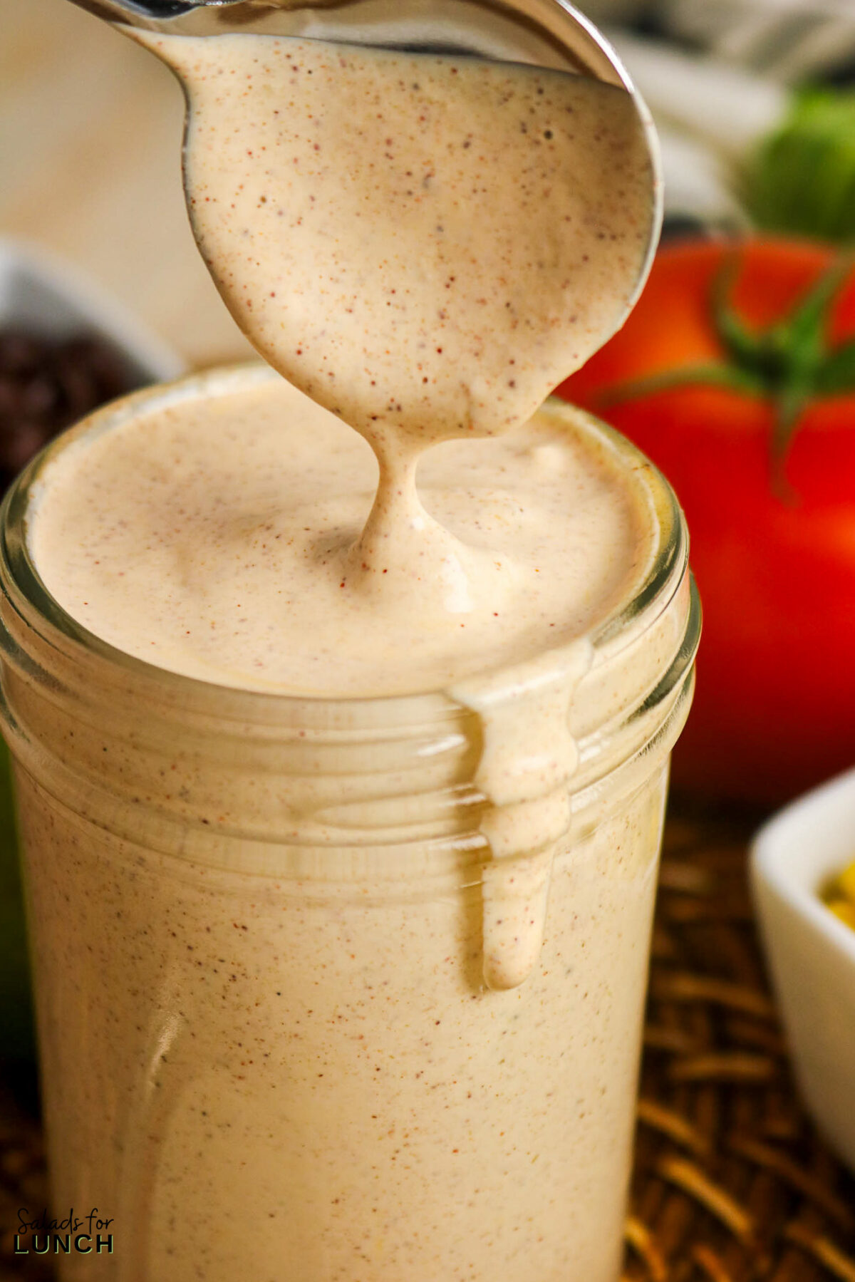 Creamy easy taco salad dressing being poured from a spoon into a jar.