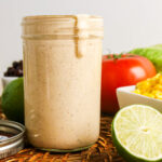 Creamy taco salad dressing in a jar with limes, tomato, corn, and black beans.