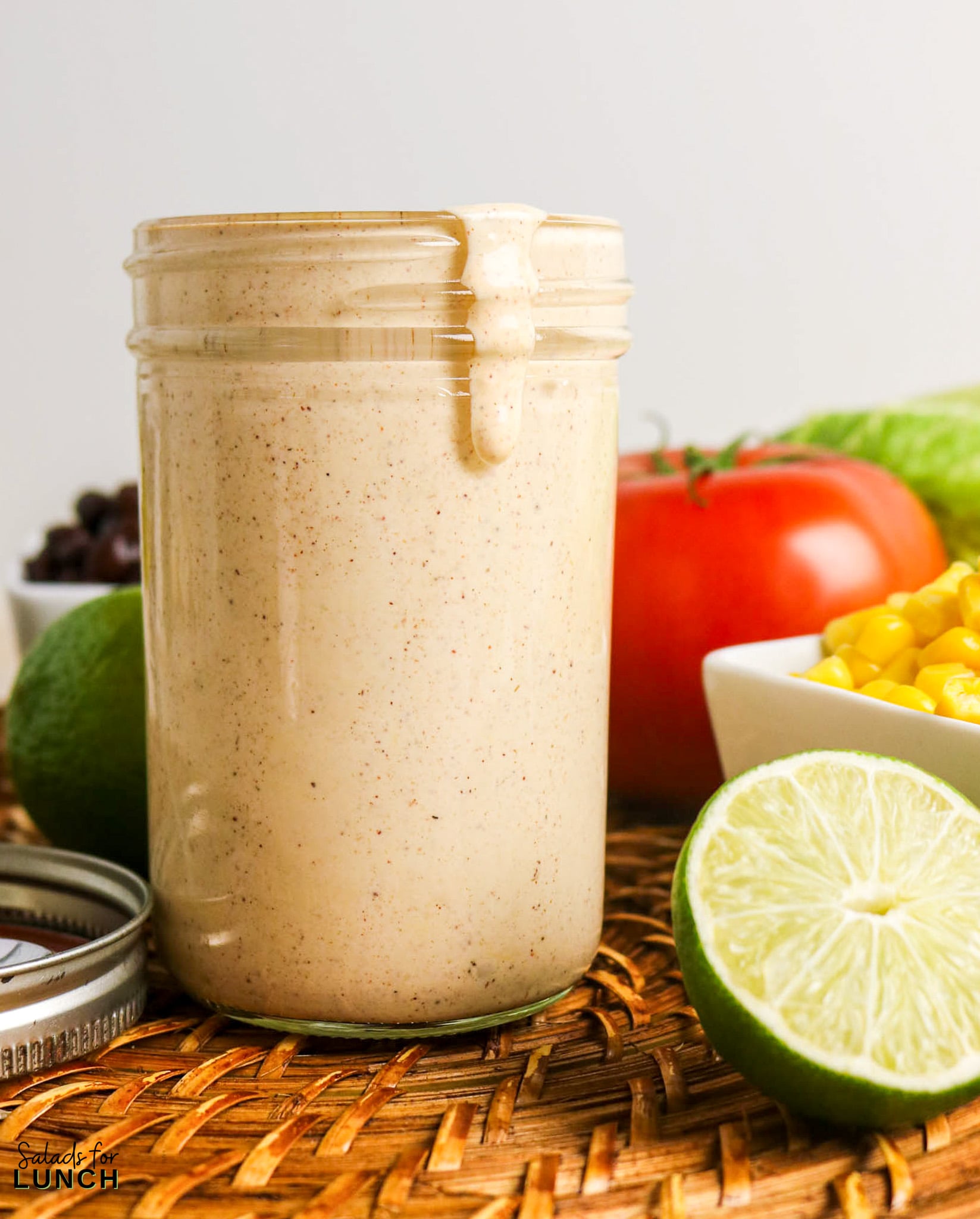 Creamy taco salad dressing in a jar with limes, tomato, corn, and black beans.