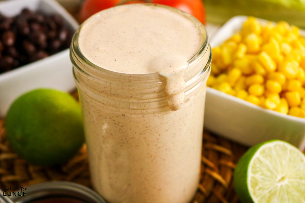Creamy easy taco salad dressing in a jar, with corn, black beans, and limes.