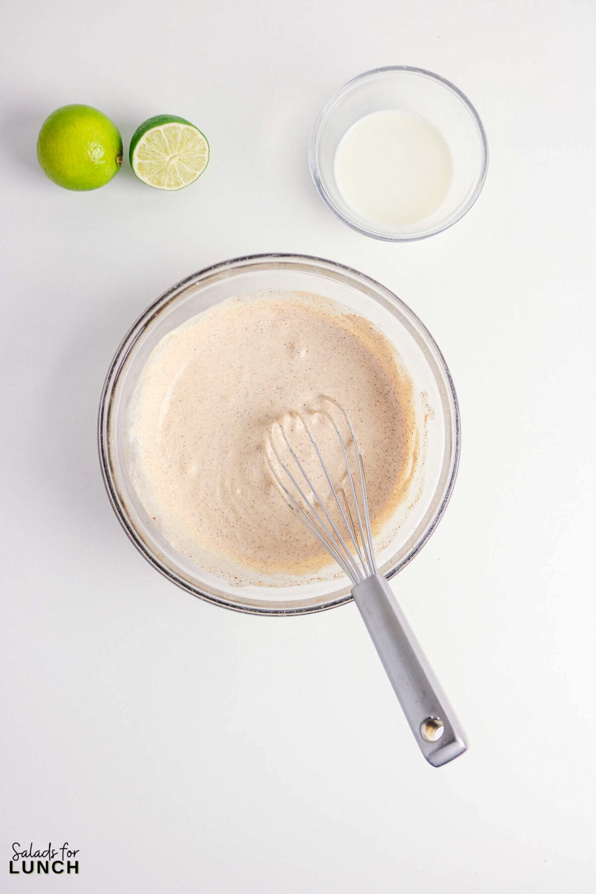 Easy taco salad dressing being whisked in a bowl with lime and milk.