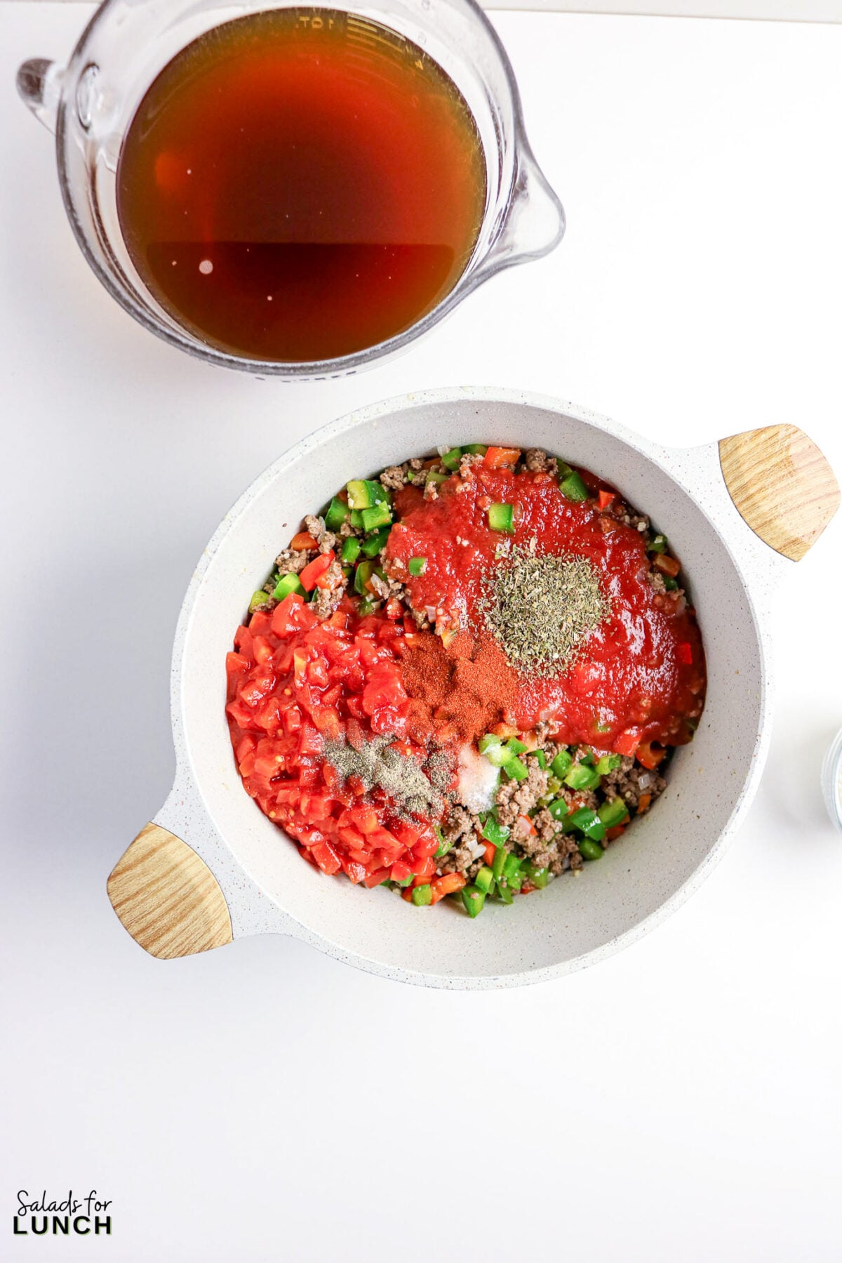 Ingredients for chili in a pot: ground beef, tomatoes, peppers, broth.