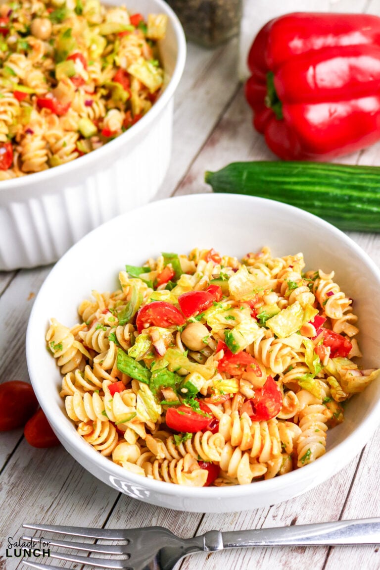 Healthy pasta salad with chickpeas, tomatoes, cucumber, and lettuce in a white bowl.